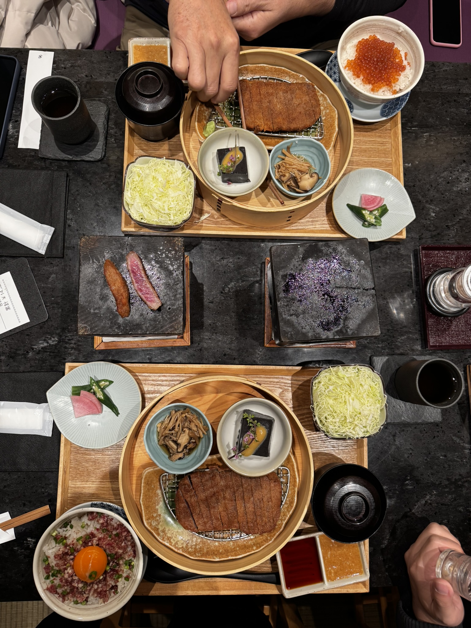 Overhead view of Gyukatsu Motomura table spread with cutlets, rice, cabbage, and hot stones