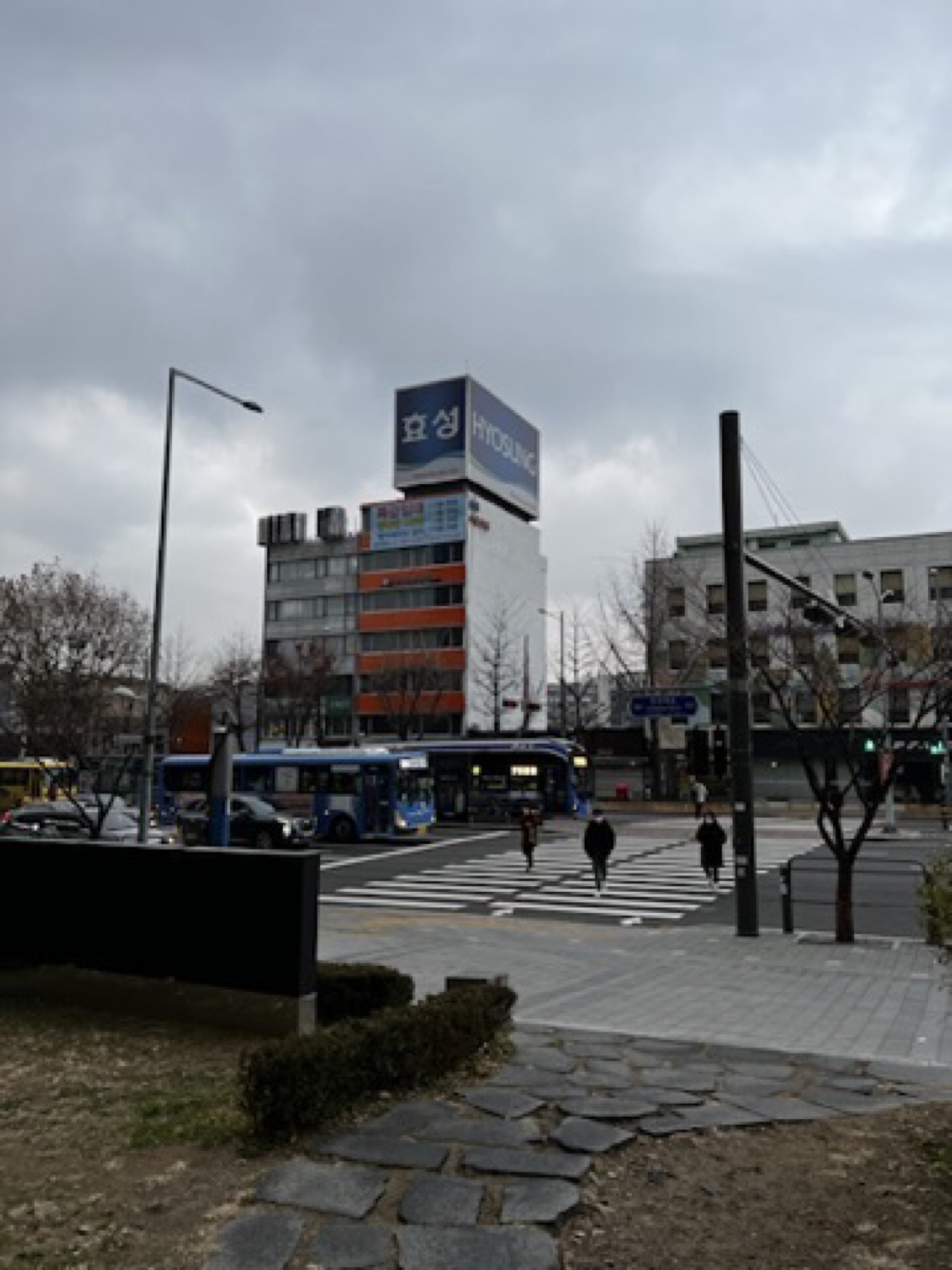 Winter street crossing in Seoul with buses, buildings, and a grey sky