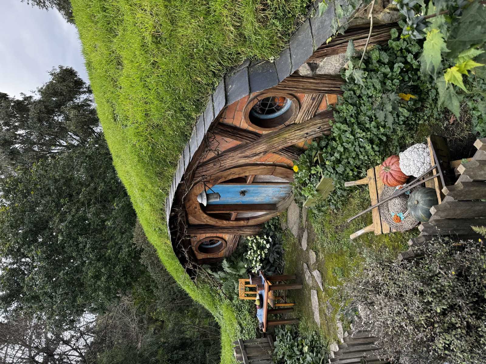 Round blue Hobbiton door set into a small hillside cottage