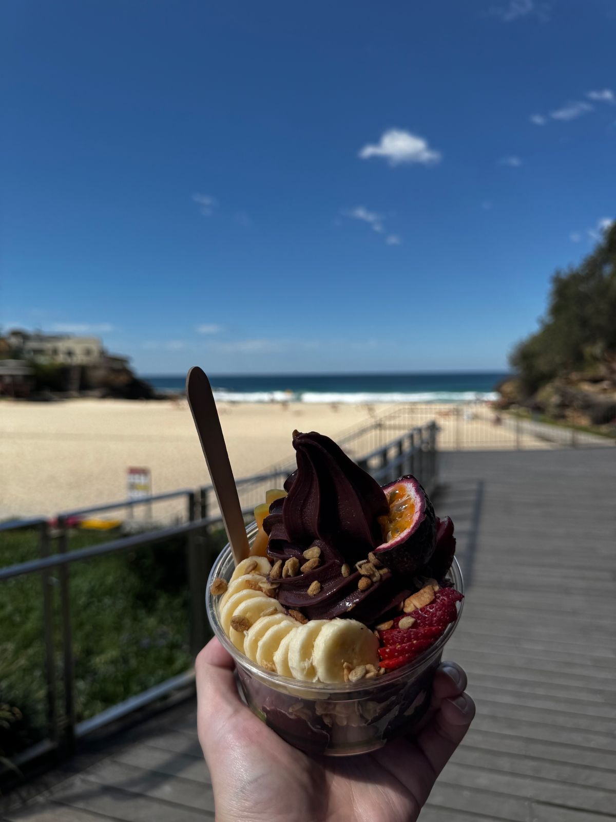 Acai bowl topped with banana, berries and chocolate sauce held up on the coastal path
