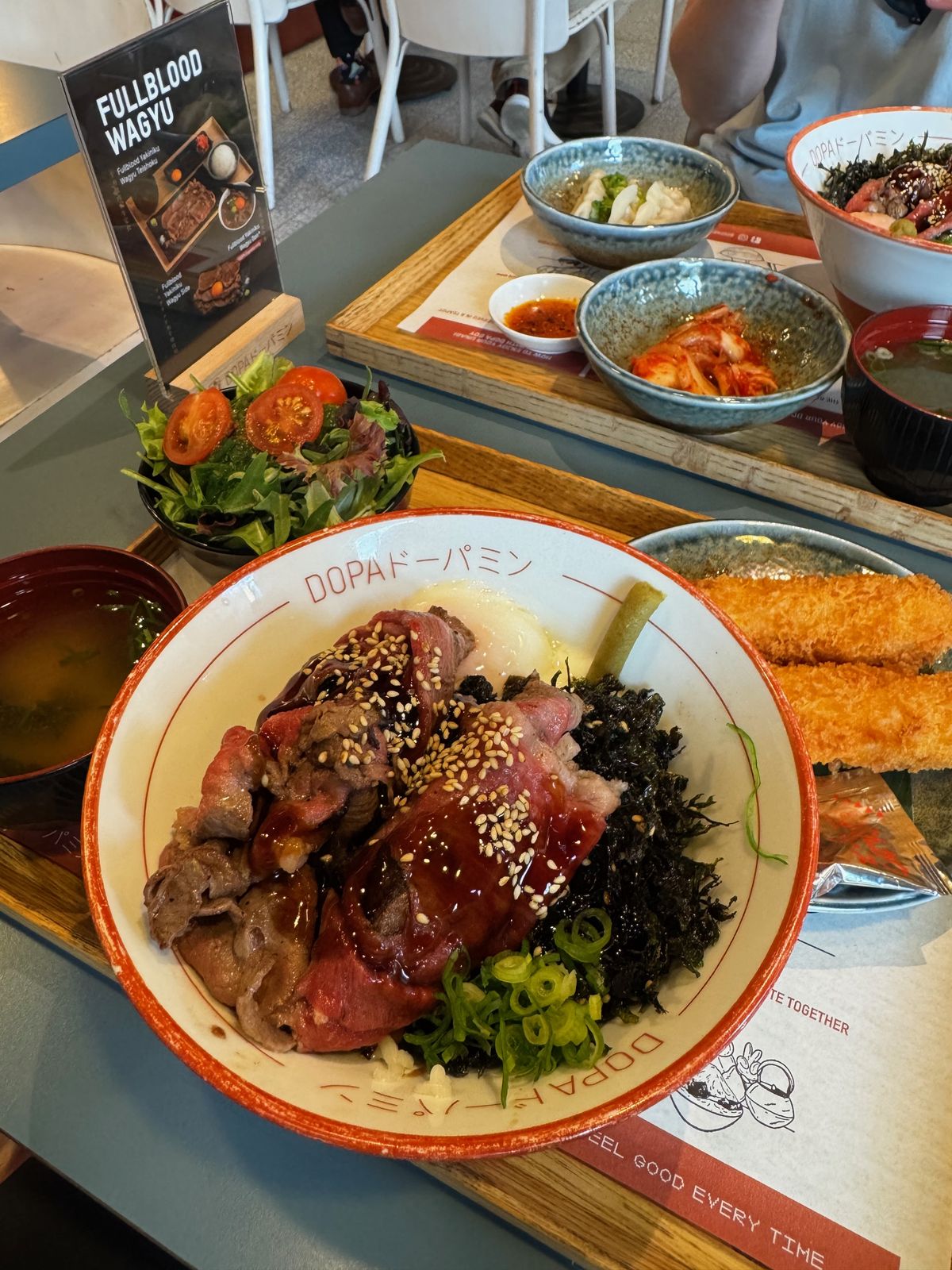 Wagyu rice bowl with sliced beef, egg yolk and pickles on a tray at DOPA