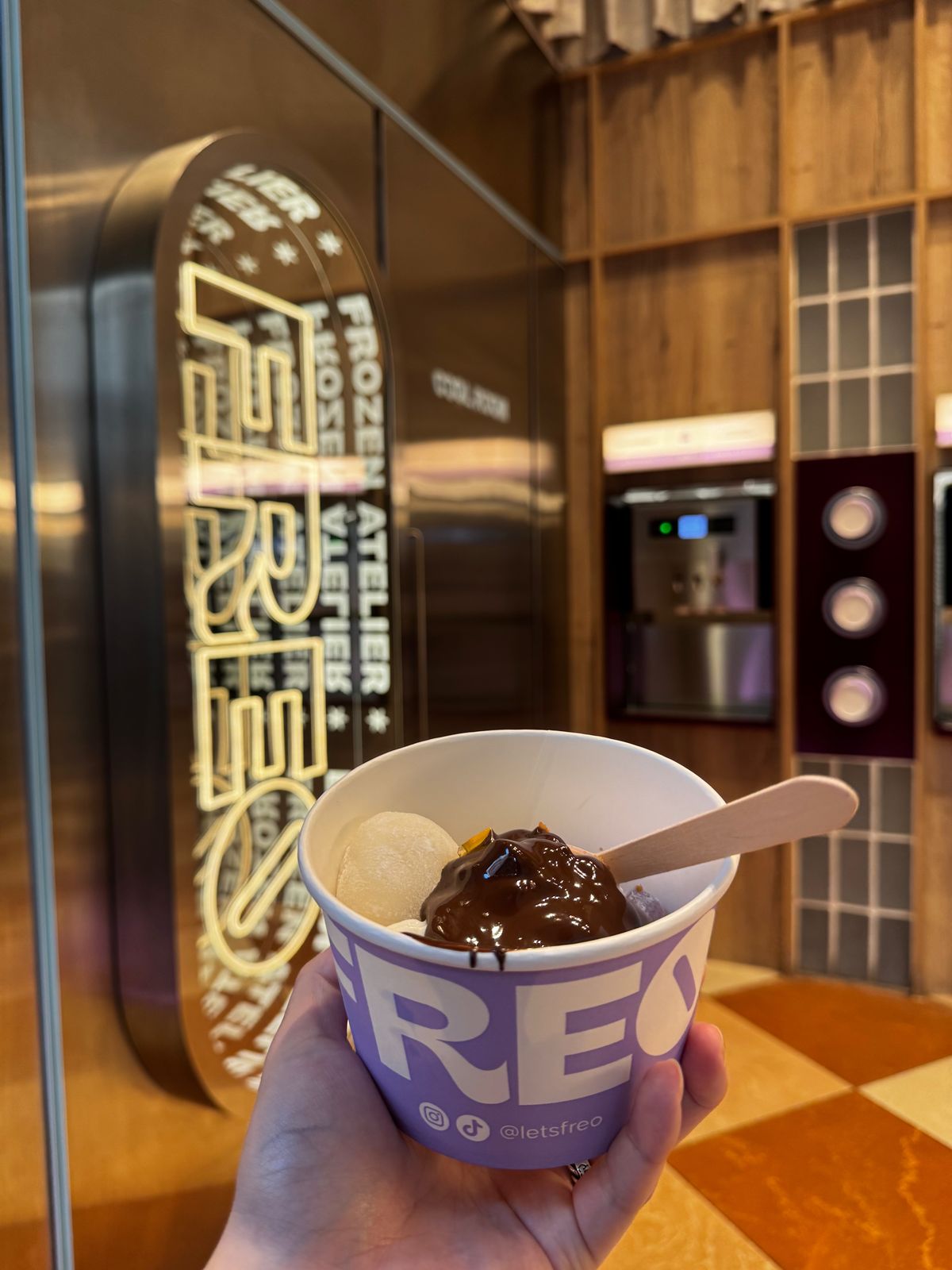 Cup of dark chocolate gelato held in front of a neon-lit gelato counter