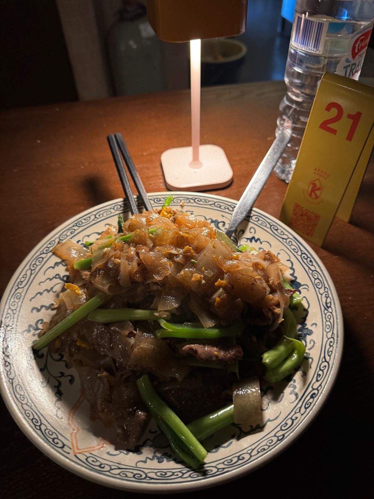 Plate of beef noodles with Chinese broccoli at a late-night restaurant table