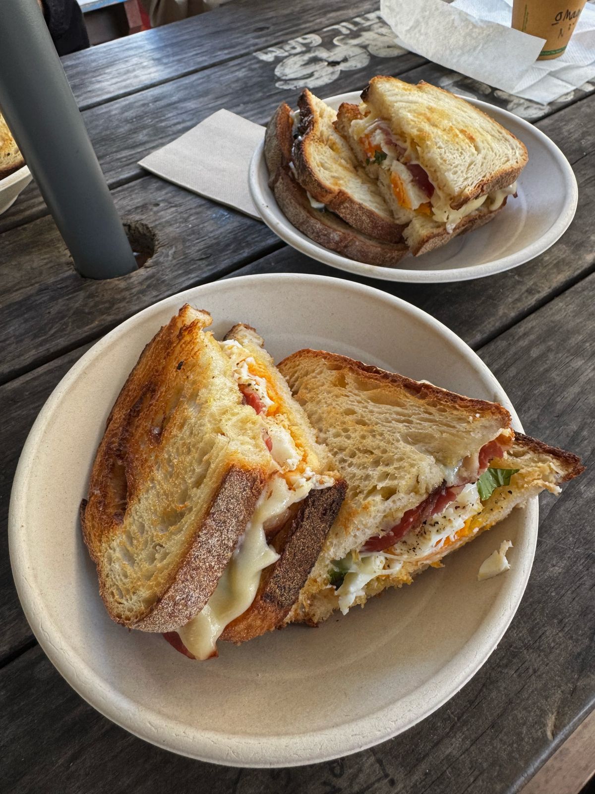 Two toasted sandwiches on plates at a wooden table