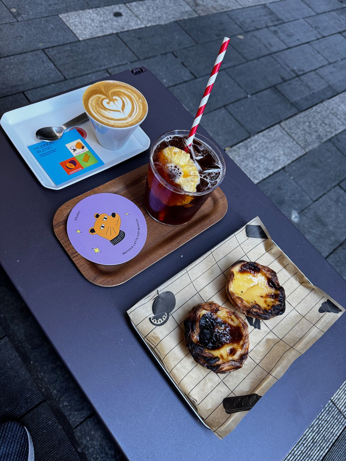 Latte with rosetta art, iced coffee and two egg tarts on a tray