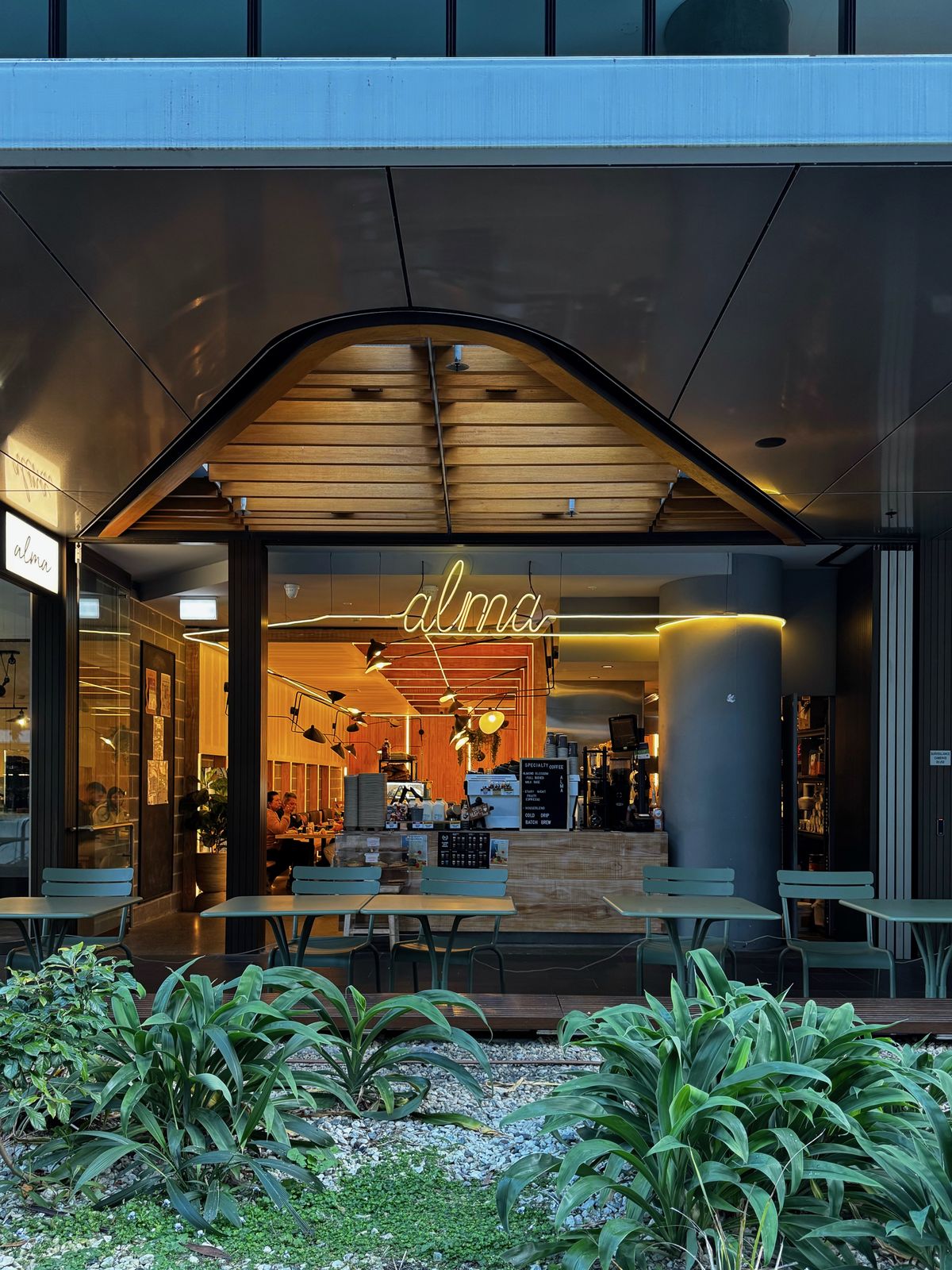 Entrance to Alma cafe with planting outside and warm lighting inside