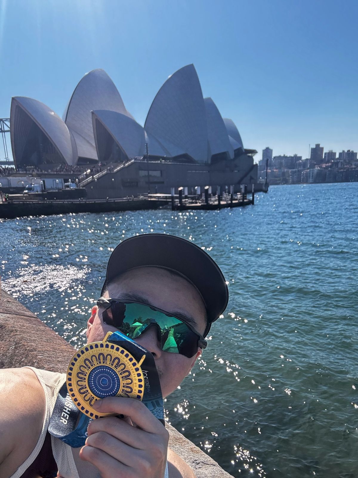 Finisher selfie holding a TCS Sydney Marathon medal by the water with the Opera House behind