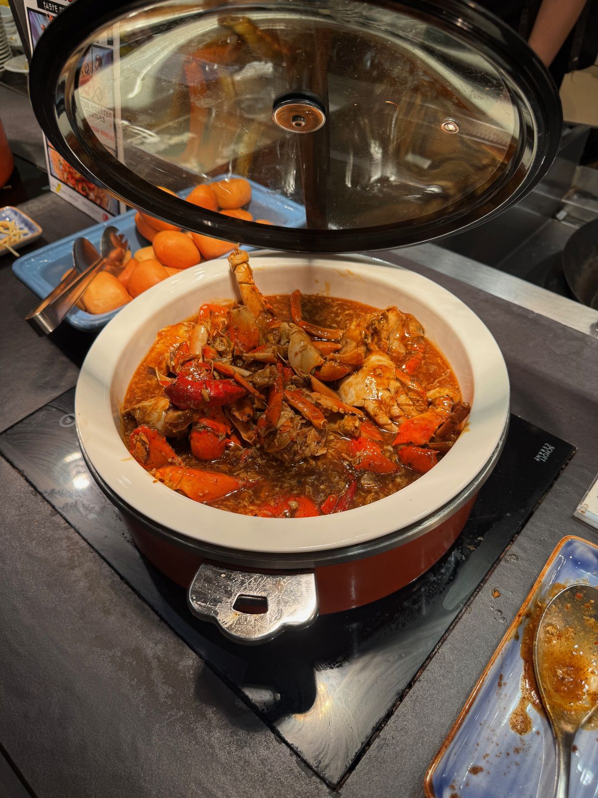 Copper pot of seafood in a red broth on a hotel buffet counter