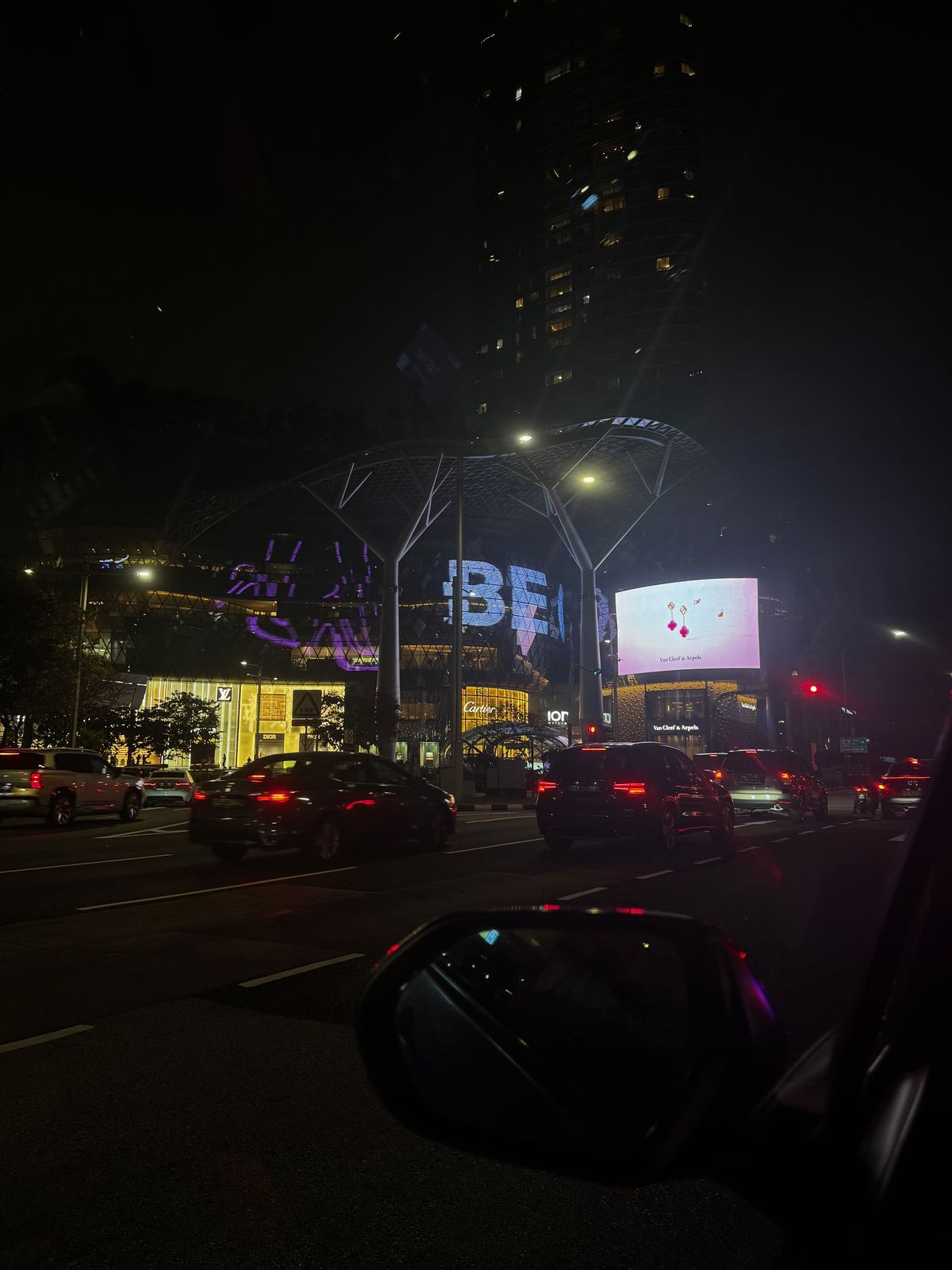 Orchard Road at night seen through a car window, lit shopfronts and traffic
