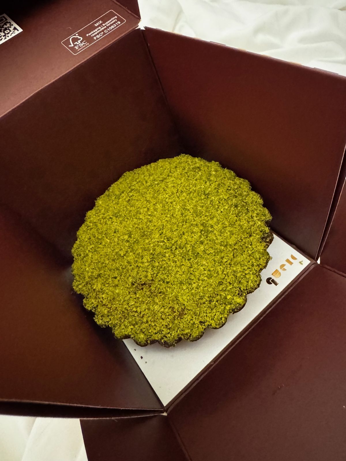 Pistachio tart in an open cake box photographed on a bed at night